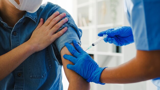 Giovane infermiera asiatica della signora che dà il vaccino antivirus Covid-19 o antinfluenzale sparato al paziente maschio anziano