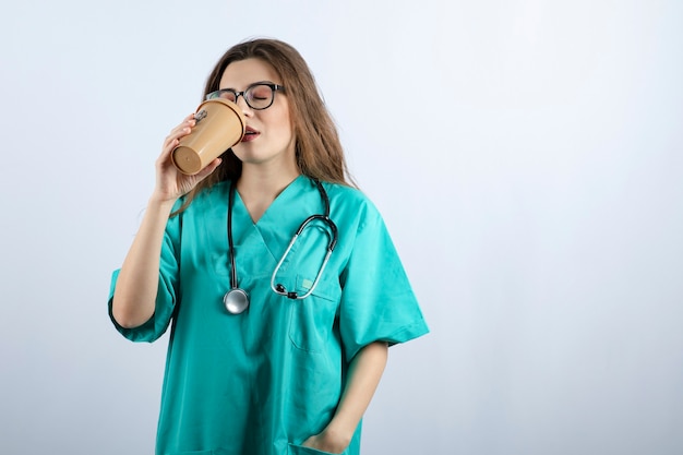 Giovane infermiera attraente con lo stetoscopio che beve da una tazza di caffè