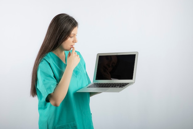 Giovane infermiera femminile che esamina computer portatile su bianco.