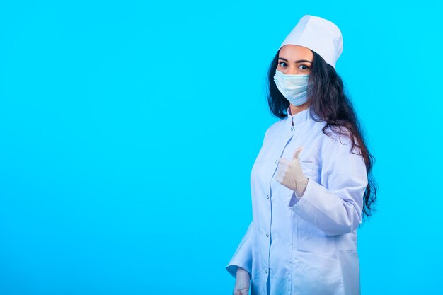 Giovane infermiera in tenuta uniforme isolata che fa i pollici aumenta il segno della mano.