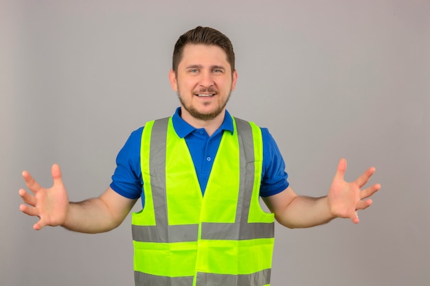 Giovane ingegnere uomo che indossa il giubbotto di costruzione gesticolando con le mani che mostrano grandi e grandi dimensioni segno misura simbolo sorridente guardando la telecamera su sfondo bianco isolato