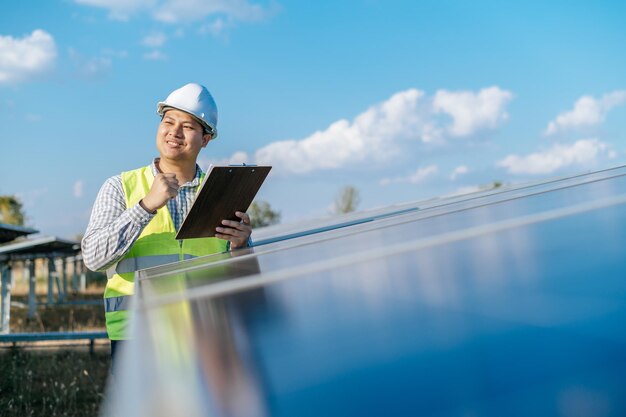 Giovane ispettore asiatico ingegnere uomo che lavora presso una fattoria solare Tecnico o supervisore maschio con casco bianco Controllo del funzionamento del sole e del pannello solare fotovoltaico nello spazio di copia della stazione