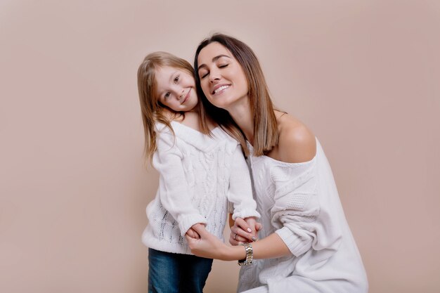 Giovane madre allegra guarda la telecamera, fischietta e abbraccia una figlia