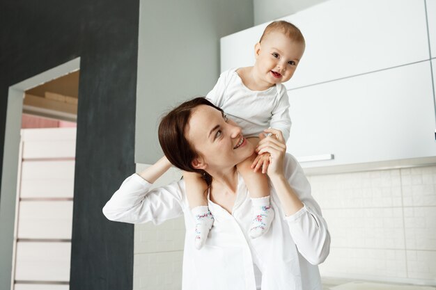 Giovane madre allegra portando il suo bambino sulle spalle e ridendo