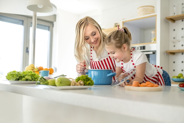 Giovane madre caucasica e figlia che indossano grembiuli abbinati cucinare la zuppa insieme in una cucina