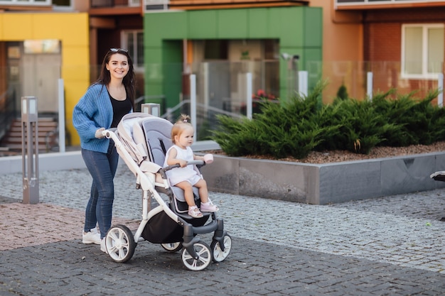 Giovane madre che cammina con il suo bambino e lo porta in una bellissima carrozzina. Felicità.