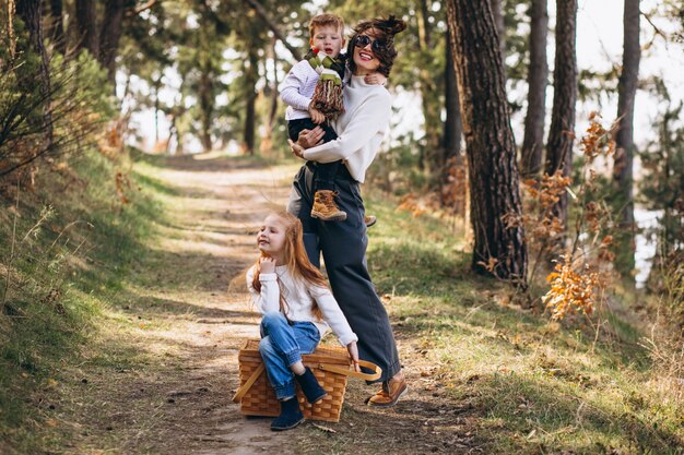 Giovane madre con la figlia e il figlio che camminano per il picnic nella foresta