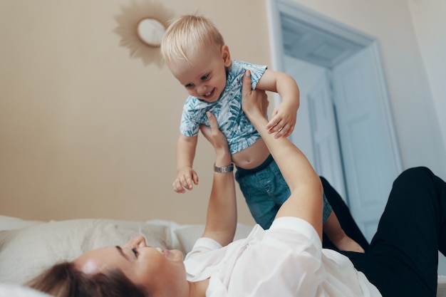 Giovane madre divertirsi ridendo giocando divertenti giochi attivi con figlio bambino carino in camera da letto