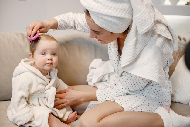 Giovane madre e bambina indossa vestaglie con i capelli avvolti in asciugamani Donna e ragazza seduta su un divano Donna che pettina i capelli di sua figlia