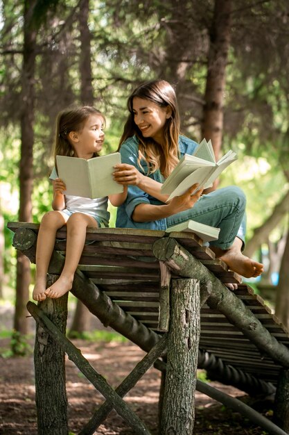 Giovane madre e figlia che leggono un libro nel bosco su un ponte di legno, il concetto di una vita familiare felice e le relazioni familiari