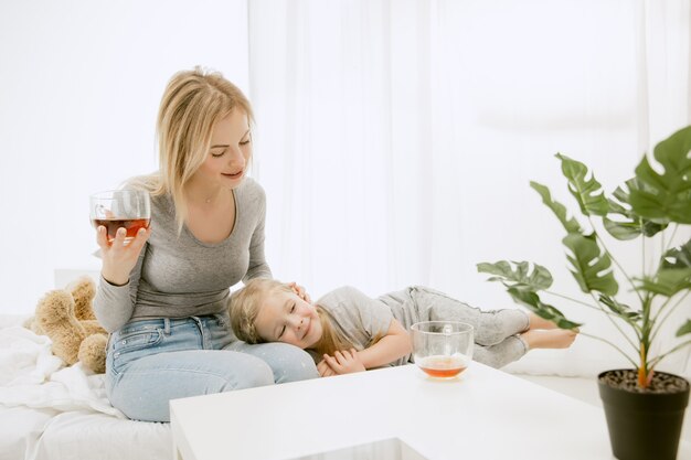 Giovane madre e la sua piccola figlia a casa al mattino pieno di sole. Colori pastello tenui. Tempo per la famiglia felice nel fine settimana. Concetto di festa della mamma. Concetti di famiglia, amore, stile di vita, maternità e momenti teneri.