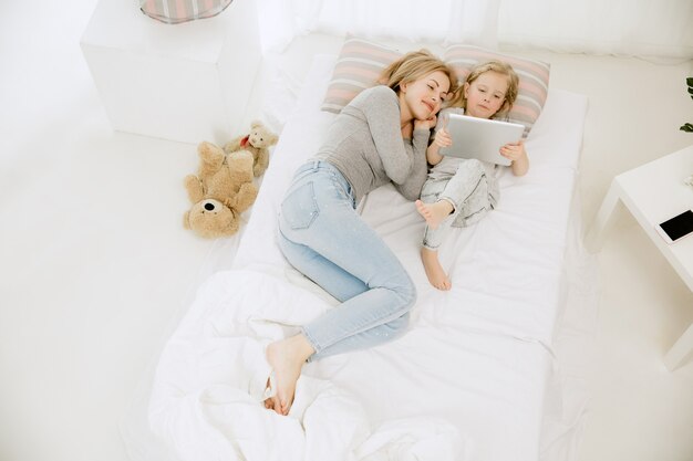 Giovane madre e la sua piccola figlia a casa al mattino pieno di sole. Colori pastello tenui. Tempo per la famiglia felice nel fine settimana. Concetto di festa della mamma. Concetti di famiglia, amore, stile di vita, maternità e momenti teneri.