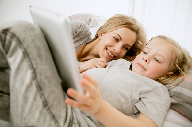 Giovane madre e la sua piccola figlia a casa al mattino pieno di sole. Colori pastello tenui. Tempo per la famiglia felice nel fine settimana. Concetto di festa della mamma. Concetti di famiglia, amore, stile di vita, maternità e momenti teneri.