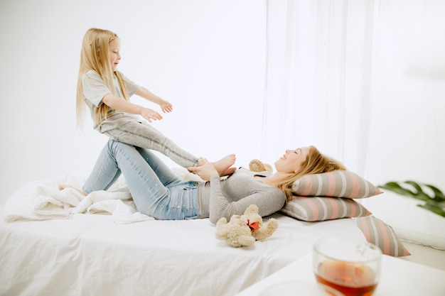 Giovane madre e la sua piccola figlia a casa al mattino pieno di sole. Colori pastello tenui. Tempo per la famiglia felice nel fine settimana. Concetto di festa della mamma. Concetti di famiglia, amore, stile di vita, maternità e momenti teneri.