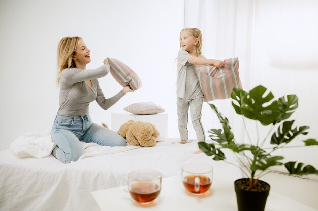 Giovane madre e la sua piccola figlia a casa al mattino pieno di sole. Colori pastello tenui. Tempo per la famiglia felice nel fine settimana. Concetto di festa della mamma. Concetti di famiglia, amore, stile di vita, maternità e momenti teneri.