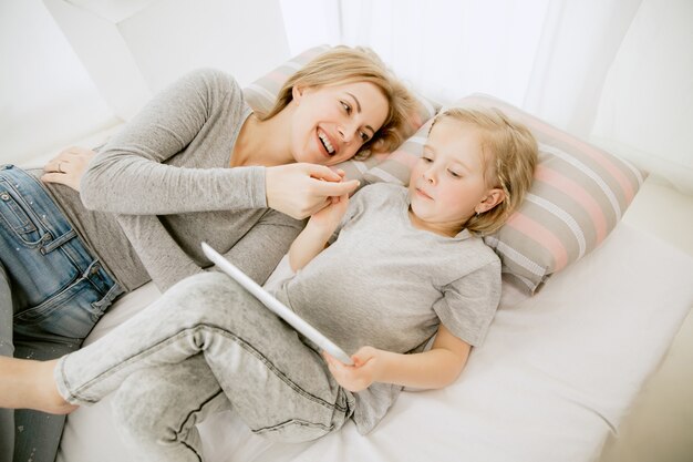 Giovane madre e la sua piccola figlia a casa al mattino pieno di sole. Colori pastello tenui. Tempo per la famiglia felice nel fine settimana. Concetto di festa della mamma. Concetti di famiglia, amore, stile di vita, maternità e momenti teneri.