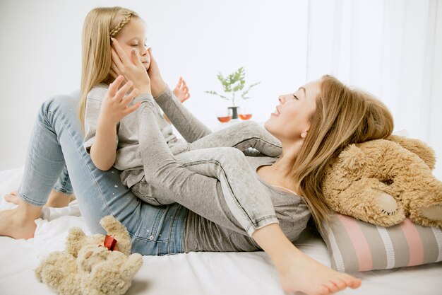 Giovane madre e la sua piccola figlia a casa al mattino pieno di sole. Colori pastello tenui. Tempo per la famiglia felice nel fine settimana. Concetto di festa della mamma