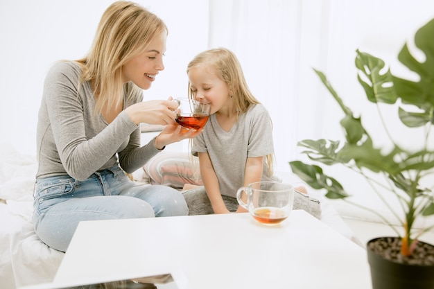 Giovane madre e la sua piccola figlia a casa al mattino pieno di sole. Colori pastello tenui. Tempo per la famiglia felice nel fine settimana. Concetto di festa della mamma