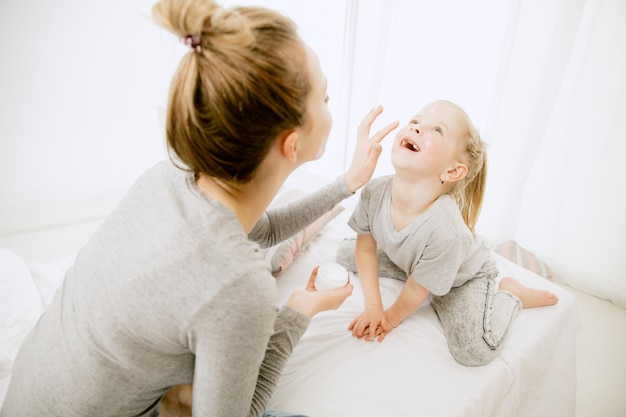 Giovane madre e la sua piccola figlia a casa al mattino pieno di sole. Colori pastello tenui. Tempo per la famiglia felice nel fine settimana. Concetto di festa della mamma