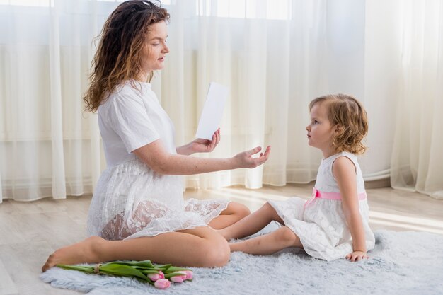 Giovane madre e sua figlia dolce che si siedono sul tappeto a casa