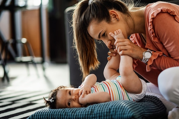 Giovane madre felice che gioca con i piccoli piedi della figlia del bambino a casa