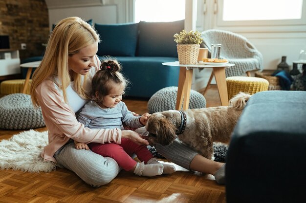 Giovane madre felice e la sua piccola figlia che si divertono con il loro cane in soggiorno