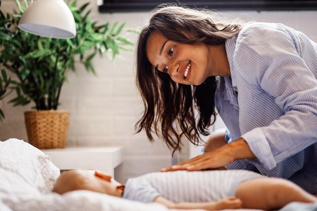 Giovane madre felice guardando il suo bambino addormentato mentre era seduto accanto al letto a casa