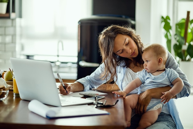 Giovane madre lavoratrice che pianifica il budget domestico mentre è con il suo bambino a casa