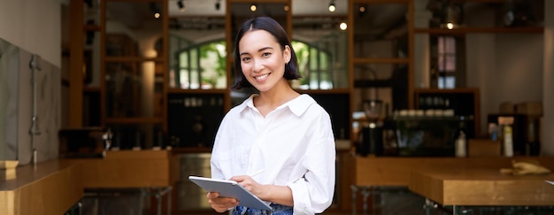 Giovane manager asiatico della caffetteria della cameriera che lavora con tablet e tavoletta grafica