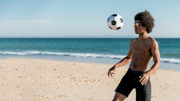 Giovane maschio afroamericano che gioca a calcio sulla spiaggia