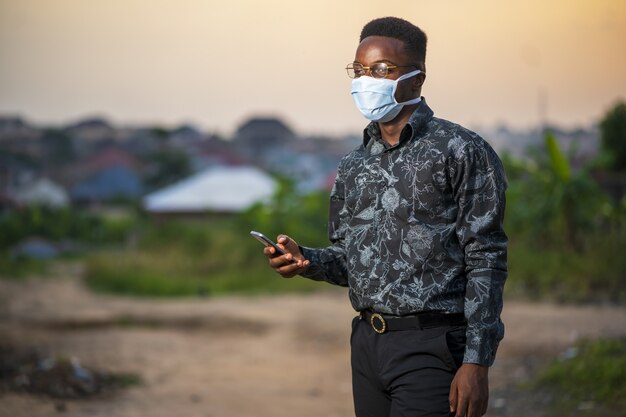 Giovane maschio afroamericano che indossa una maschera protettiva utilizzando il suo telefono all'aperto