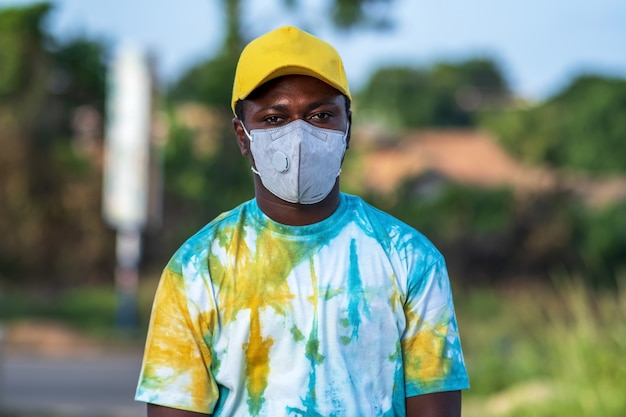 Giovane maschio afroamericano elegante in piedi all'aperto con una maschera protettiva