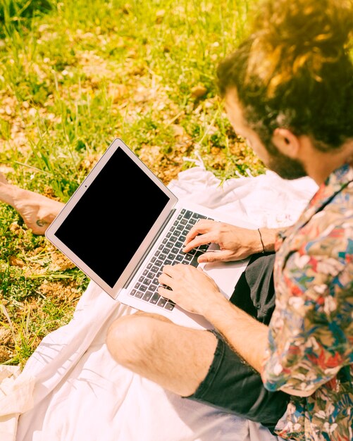 Giovane maschio barbuto che fissa al computer portatile in radura