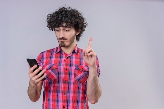 Giovane maschio capelli ricci isolato camicia colorata smartphone idea dito