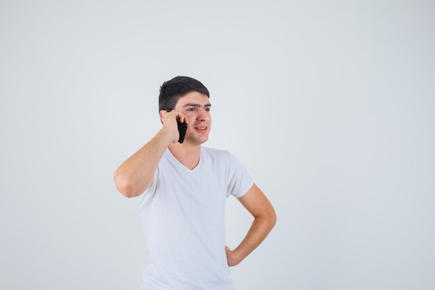 Giovane maschio che comunica sul telefono cellulare in maglietta e che sembra allegro. vista frontale.