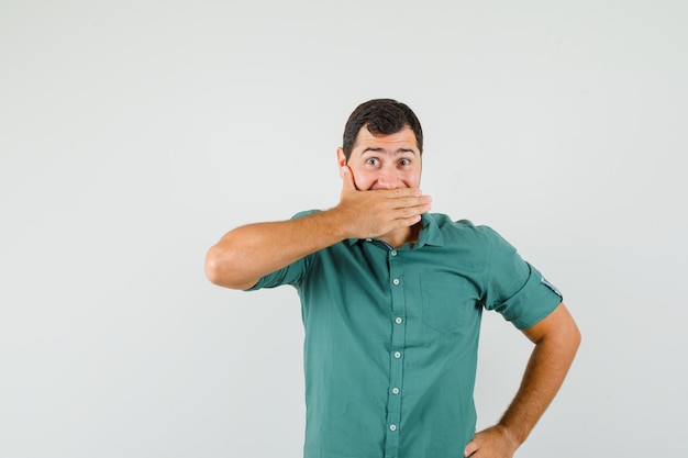 Giovane maschio che copre la bocca con la mano in camicia verde, vista frontale.