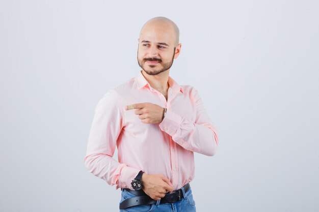 Giovane maschio che indica il lato sinistro in camicia, jeans e sembra felice. vista frontale.