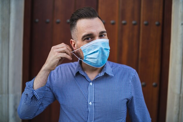 Giovane maschio che indossa una camicia blu in piedi al cancello con una maschera medica - concetto Covid-19