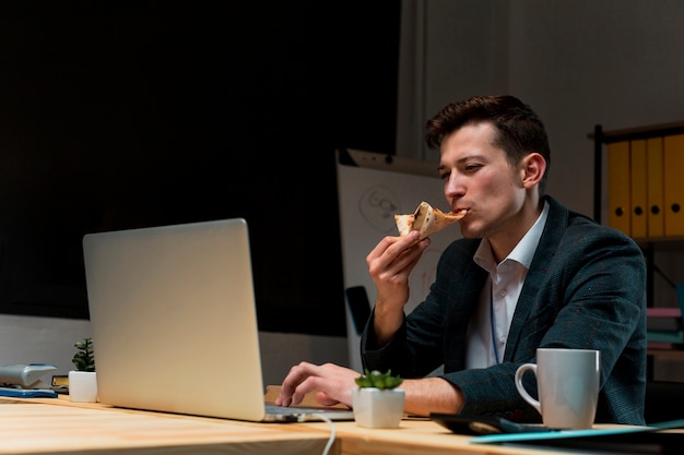 Giovane maschio che mangia uno spuntino mentre lavorando dalla casa