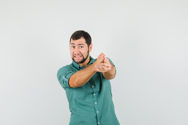 Giovane maschio che mostra il gesto della pistola di tiro in camicia verde e sembra stressante. vista frontale.