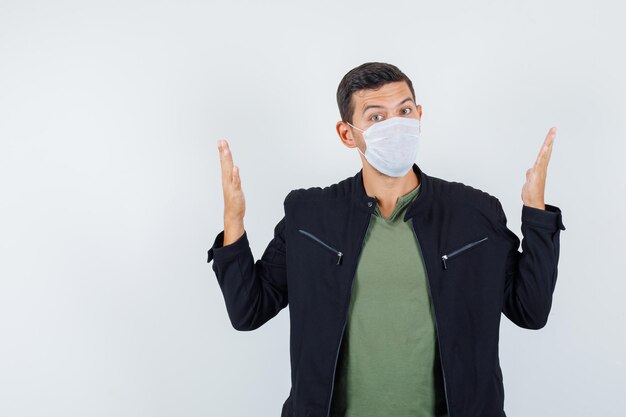 Giovane maschio che mostra il segno della taglia alzando le mani in maglietta, giacca, vista frontale della maschera.