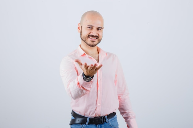 Giovane maschio che presenta qualcosa in camicia, jeans e sembra felice, vista frontale.