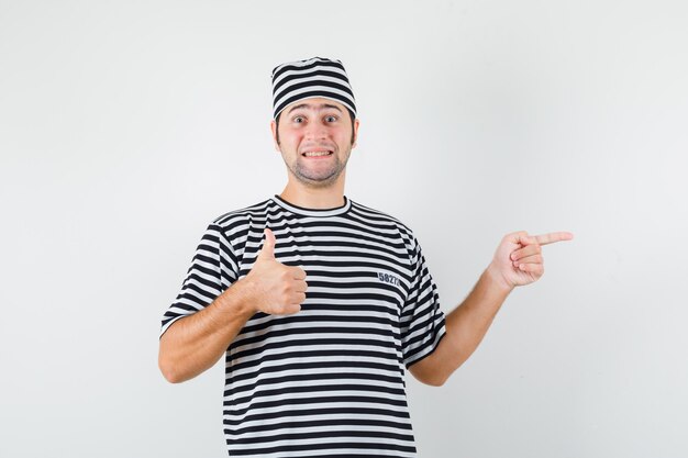 Giovane maschio che punta al lato destro, mostrando il pollice in su in t-shirt, vista frontale del cappello.