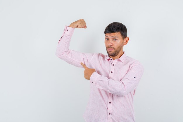 Giovane maschio che punta al suo muscolo in camicia rosa e sembra fiducioso. vista frontale.