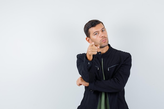 Giovane maschio che punta alla telecamera in t-shirt, giacca e sembra serio. vista frontale.