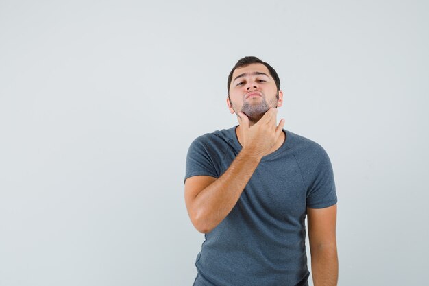 Giovane maschio che si strofina la barba in maglietta grigia e che sembra bello