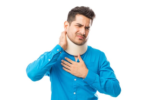 Giovane maschio che soffre di collo mentre indossa il collare cervicale su sfondo bianco