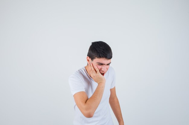 Giovane maschio che soffre di mal di denti in t-shirt e sembra doloroso, vista frontale.