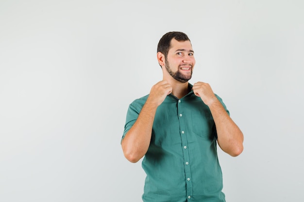 Giovane maschio che tiene il colletto in camicia verde e sembra felice, vista frontale.