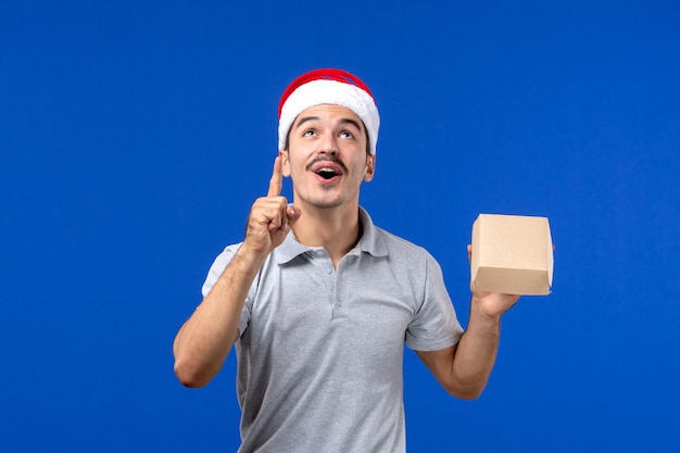 Giovane maschio che tiene pacchetto dell'alimento di vista frontale sul lavoro di servizio maschio dell'alimento della parete blu